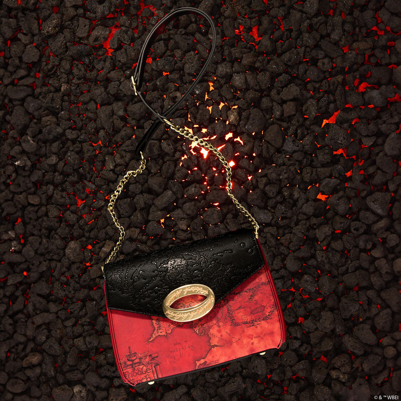 Loungefly Lord of the Rings crossbody bag featuring a red body and black top flap with a map of Middle Earth all over it. The top flap had a metal charm of the One Ring on it. The bag sits against a background of glowing coals.